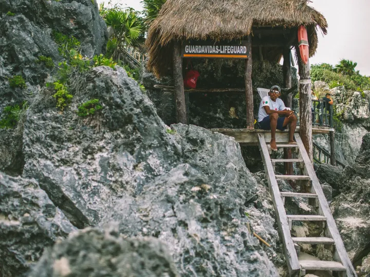 Small hut perched on rocky cliffs above bright coastal water