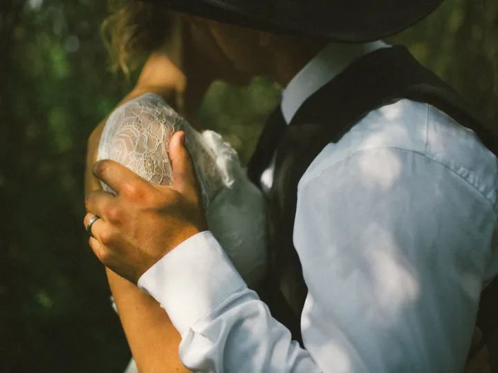 Close-up of a groom in a cowboy hat embracing a bride, wedding band visible on his hand