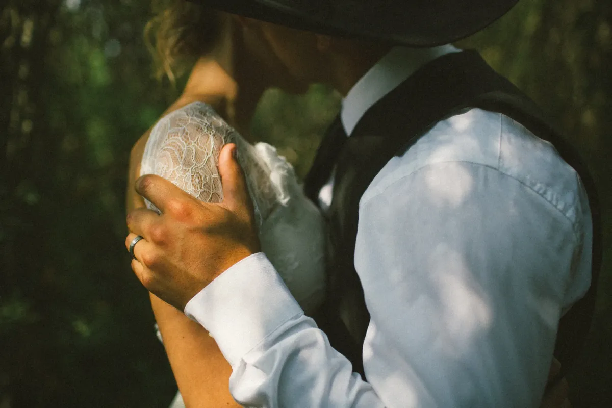 Close-up of a groom in a cowboy hat embracing a bride, wedding band visible on his hand