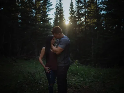Couple holding each other in dark forest light near sunset
