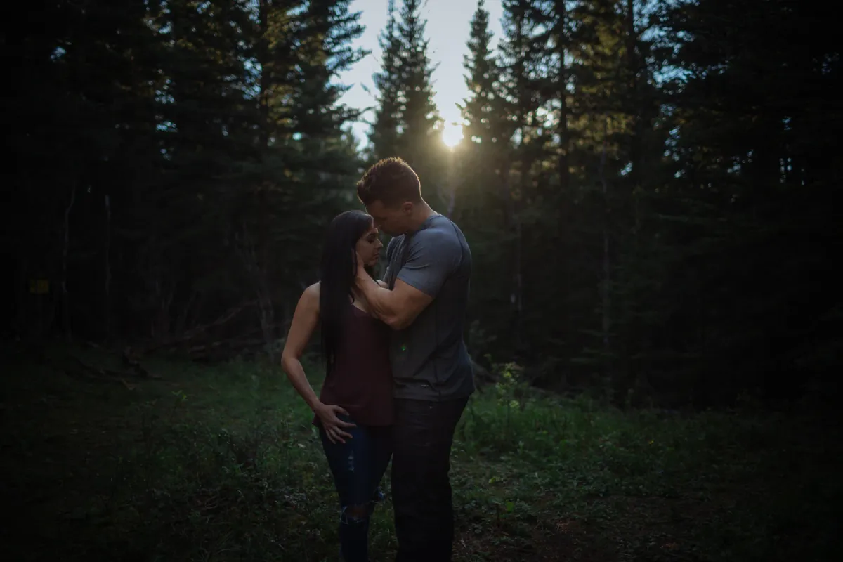 Couple holding each other in dark forest light near sunset