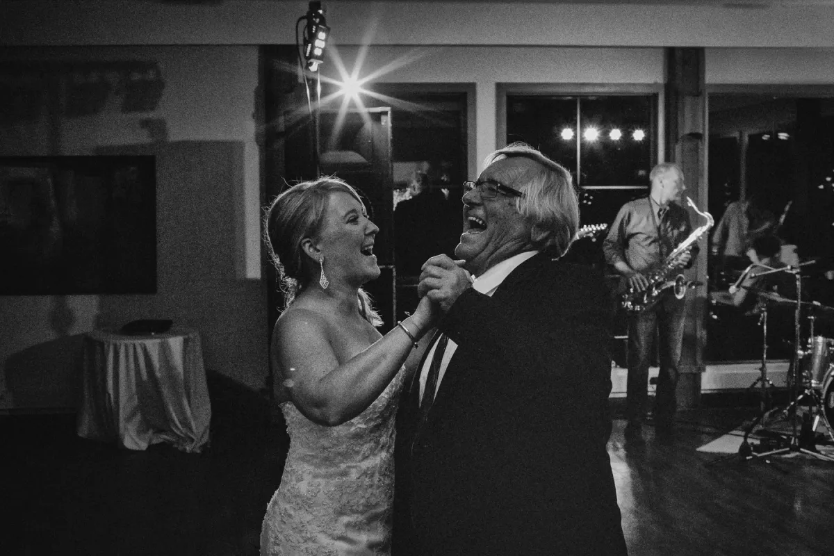Black and white photo of a bride and older man laughing while dancing at a wedding reception