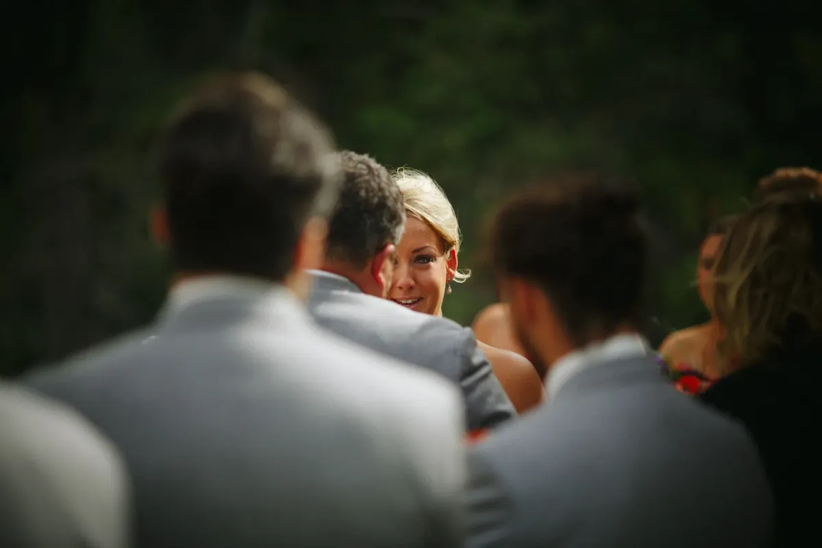 Candid close-up of a blonde bride's face framed by blurred guests during an outdoor ceremony