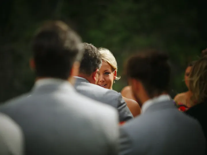 Candid close-up of a blonde bride's face framed by blurred guests during an outdoor ceremony