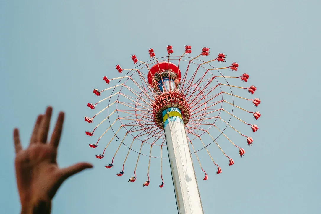 Hand reaching toward a colourful amusement ride against the sky
