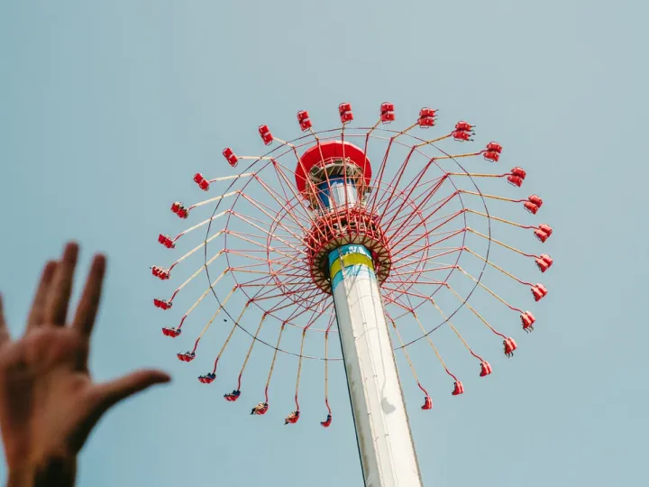 Hand reaching toward a colourful amusement ride against the sky