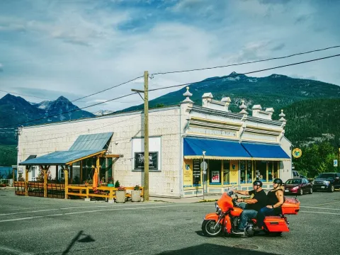 Small mountain town storefront with people riding past under a blue sky
