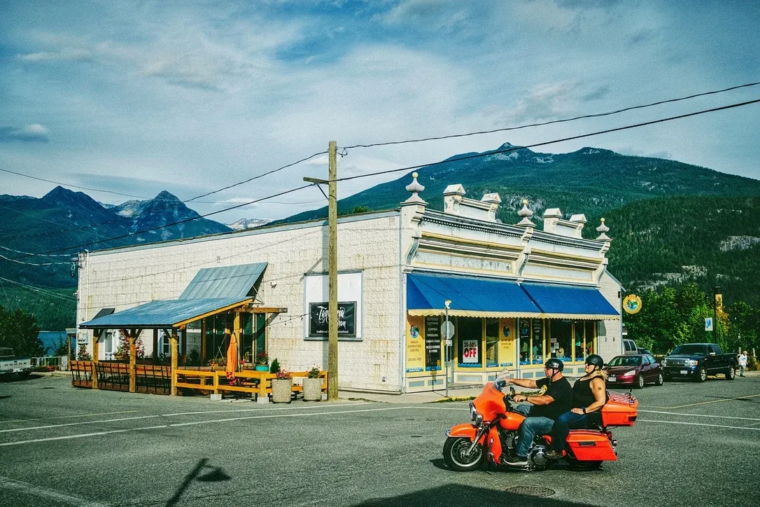 Small mountain town storefront with people riding past under a blue sky