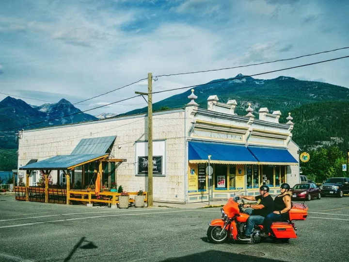 Small mountain town storefront with people riding past under a blue sky
