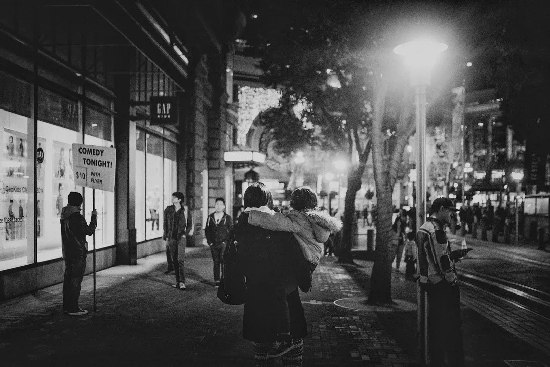 Black-and-white city street scene at night with people waiting under streetlights