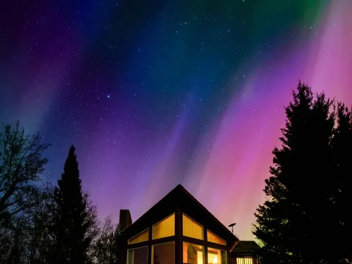 Cabin glowing beneath northern lights in a dark sky