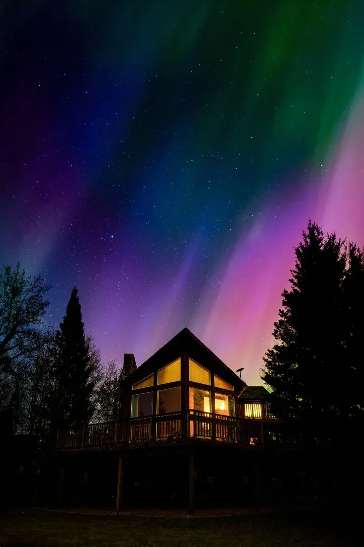 Cabin glowing beneath northern lights in a dark sky