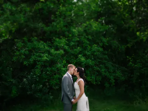 Bride and groom kissing in profile against a dense background of green foliage