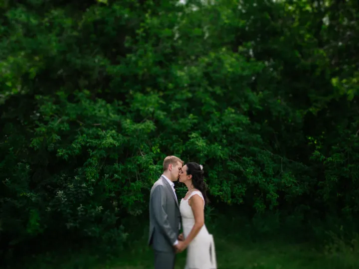 Bride and groom kissing in profile against a dense background of green foliage