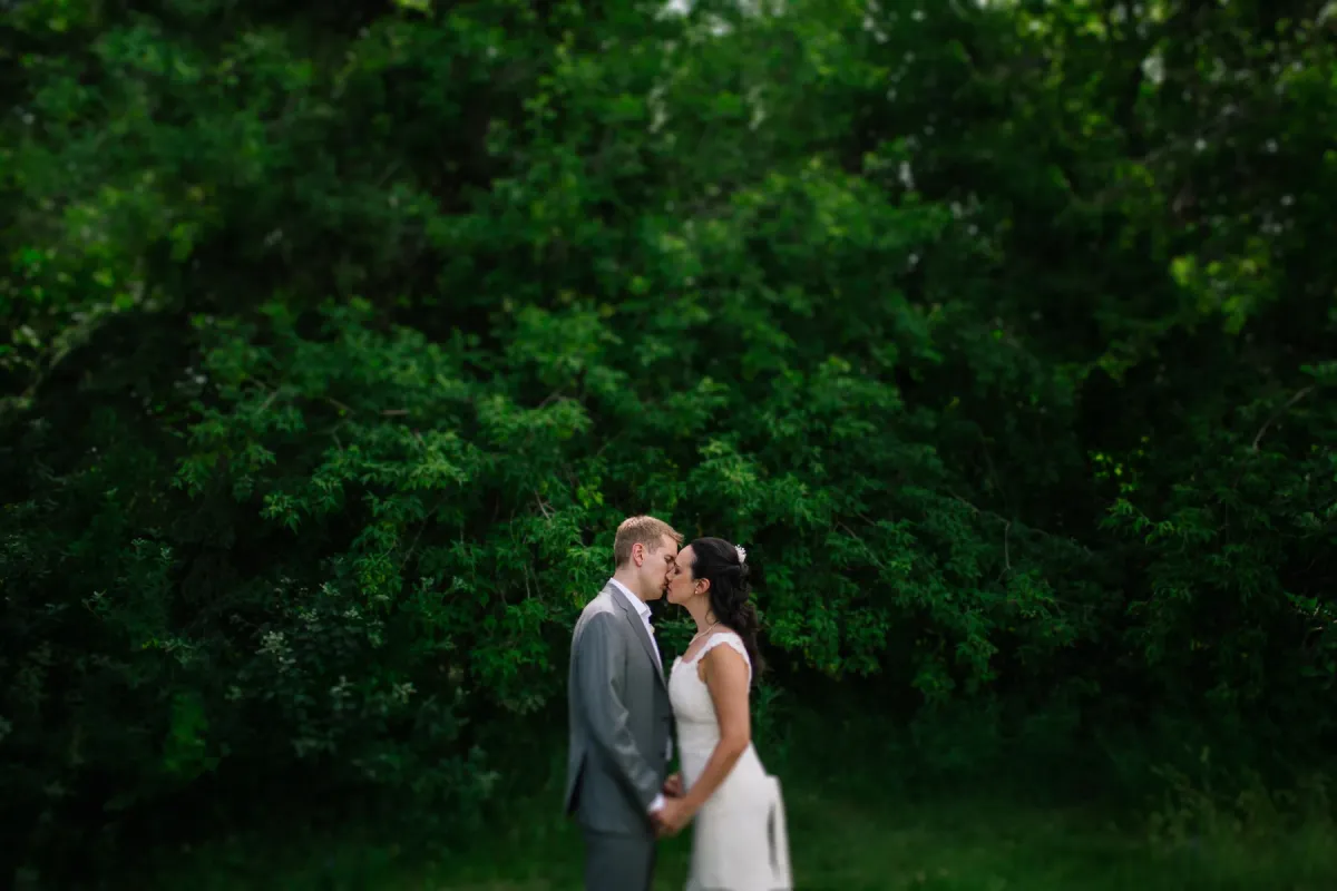 Bride and groom kissing in profile against a dense background of green foliage