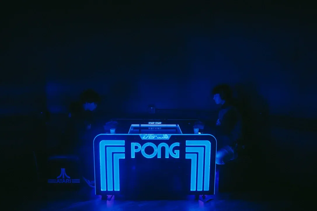 Blue neon Pong arcade sign glowing in a dark room