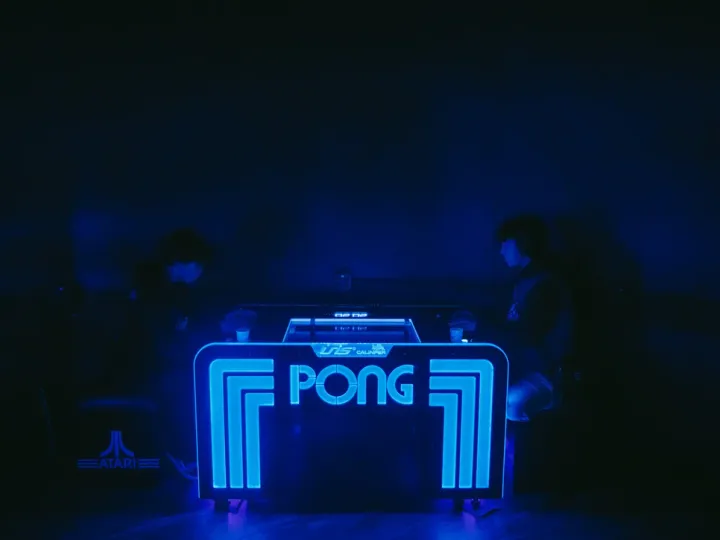 Blue neon Pong arcade sign glowing in a dark room