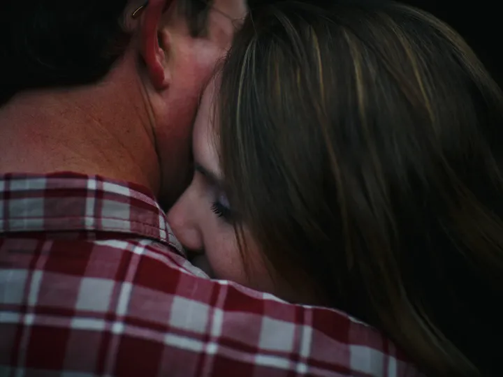 Couple holding close with a quiet kiss at the shoulder during an engagement session
