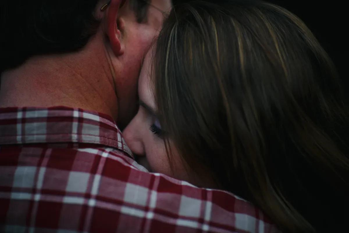 Couple holding close with a quiet kiss at the shoulder during an engagement session