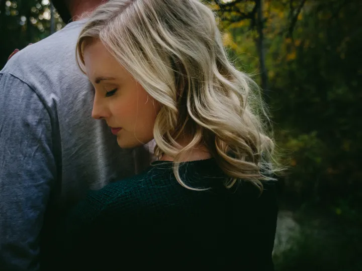 Close engagement portrait of a woman leaning against her partner in soft forest light