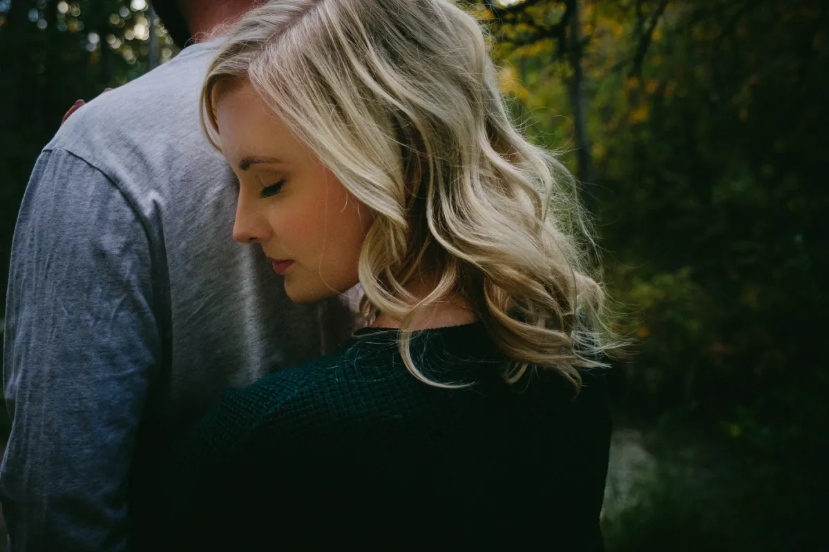 Close engagement portrait of a woman leaning against her partner in soft forest light