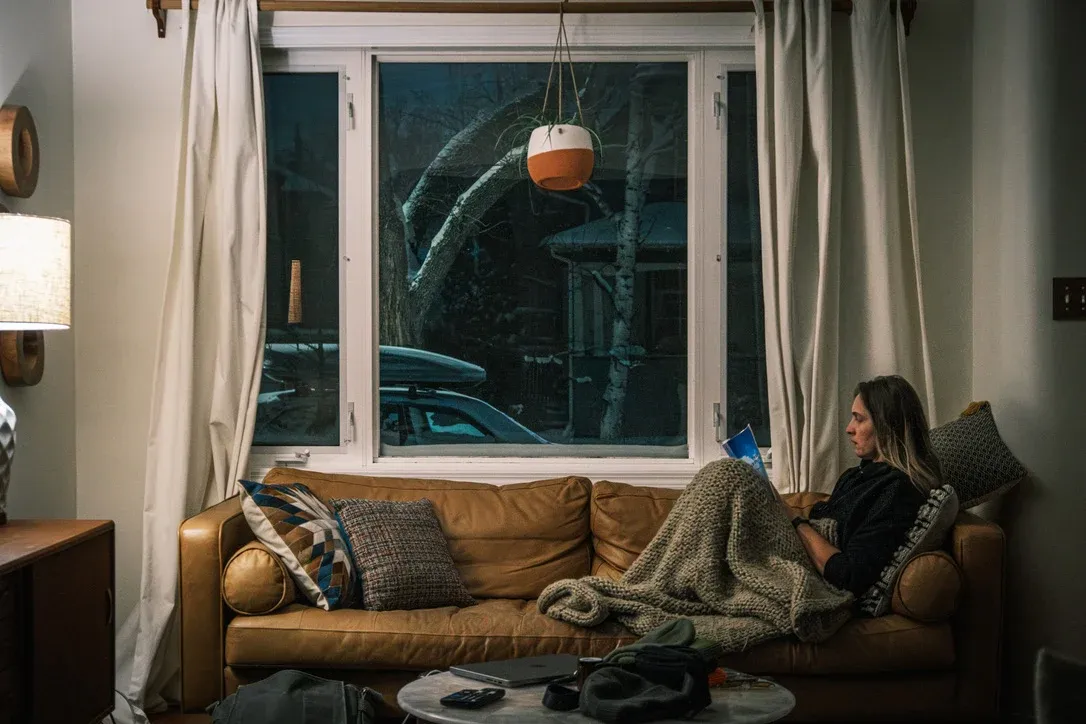 Person reading on a couch beside a winter window while travelling