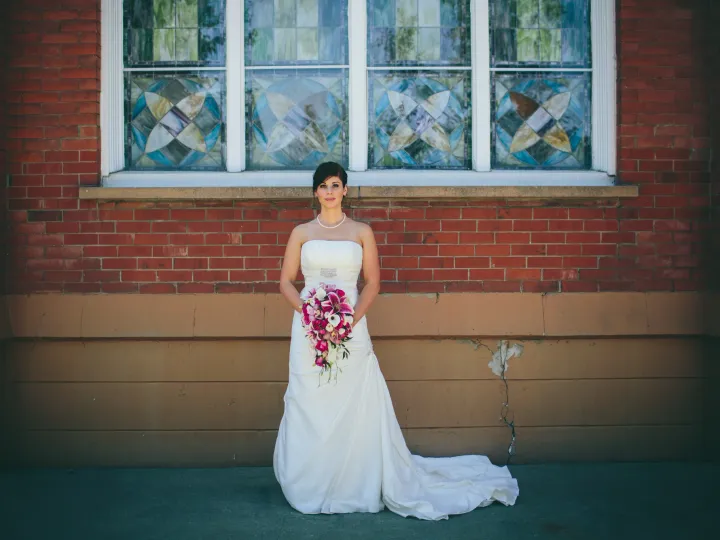 Bride standing against a red brick wall in a white dress