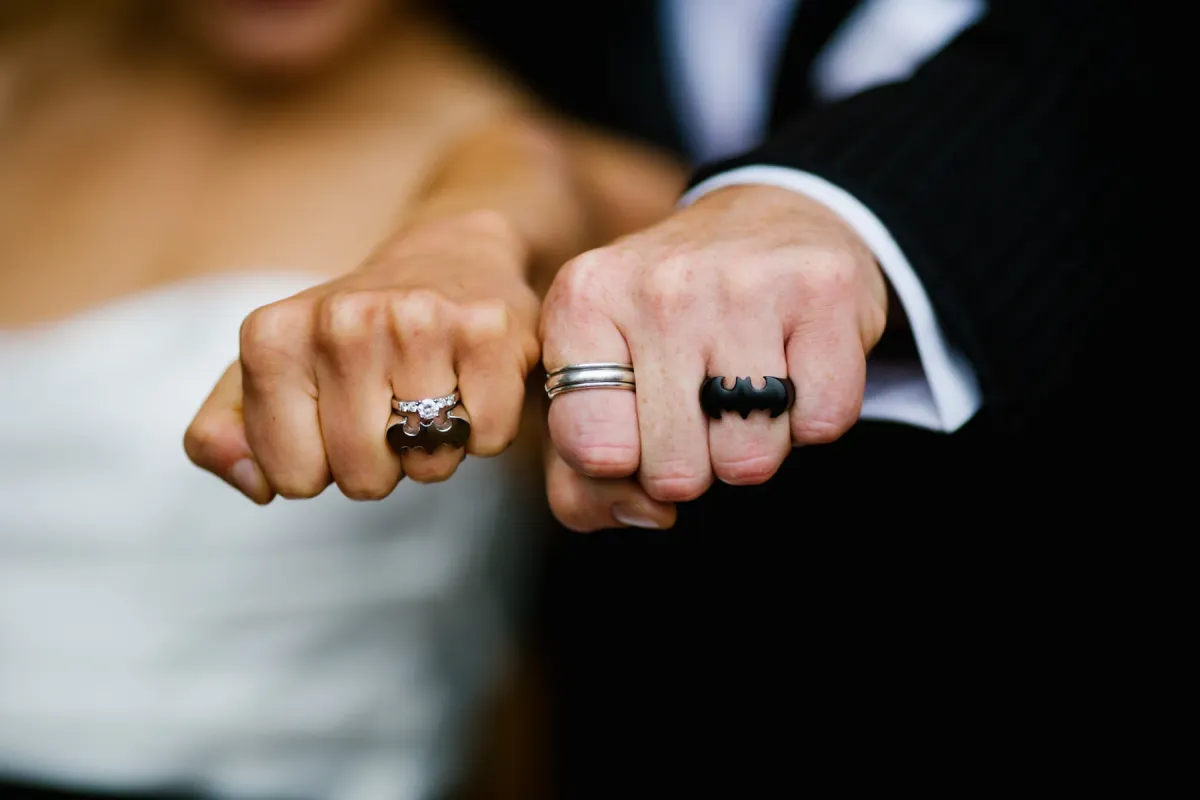 Close-up of bride and groom fists showing diamond and Batman-themed wedding rings