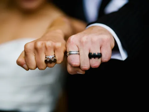 Close-up of bride and groom fists showing diamond and Batman-themed wedding rings
