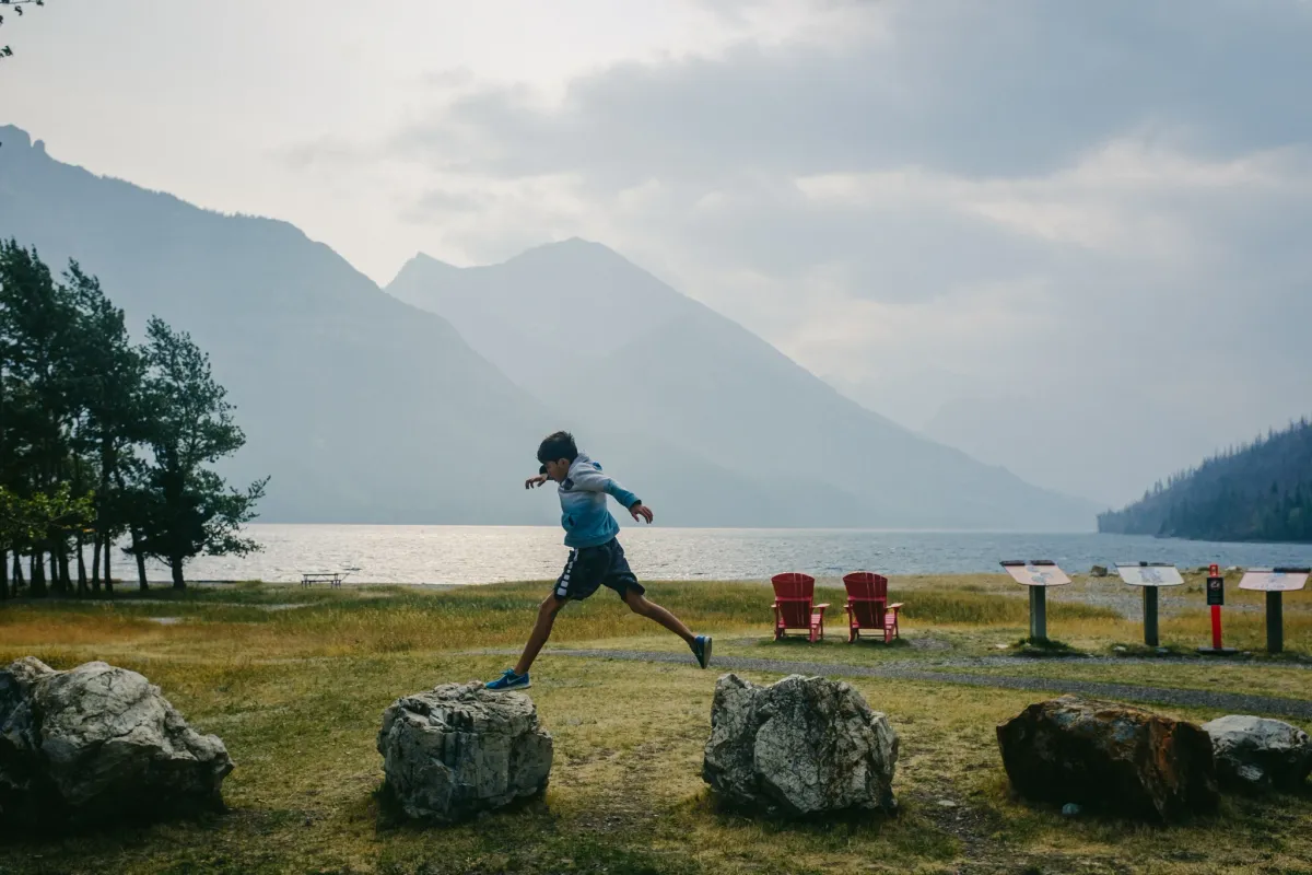 Child running across a lakeside lawn with mountains and red chairs in the distance