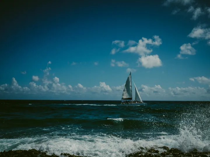 Small sailboat crossing bright blue ocean water under scattered clouds
