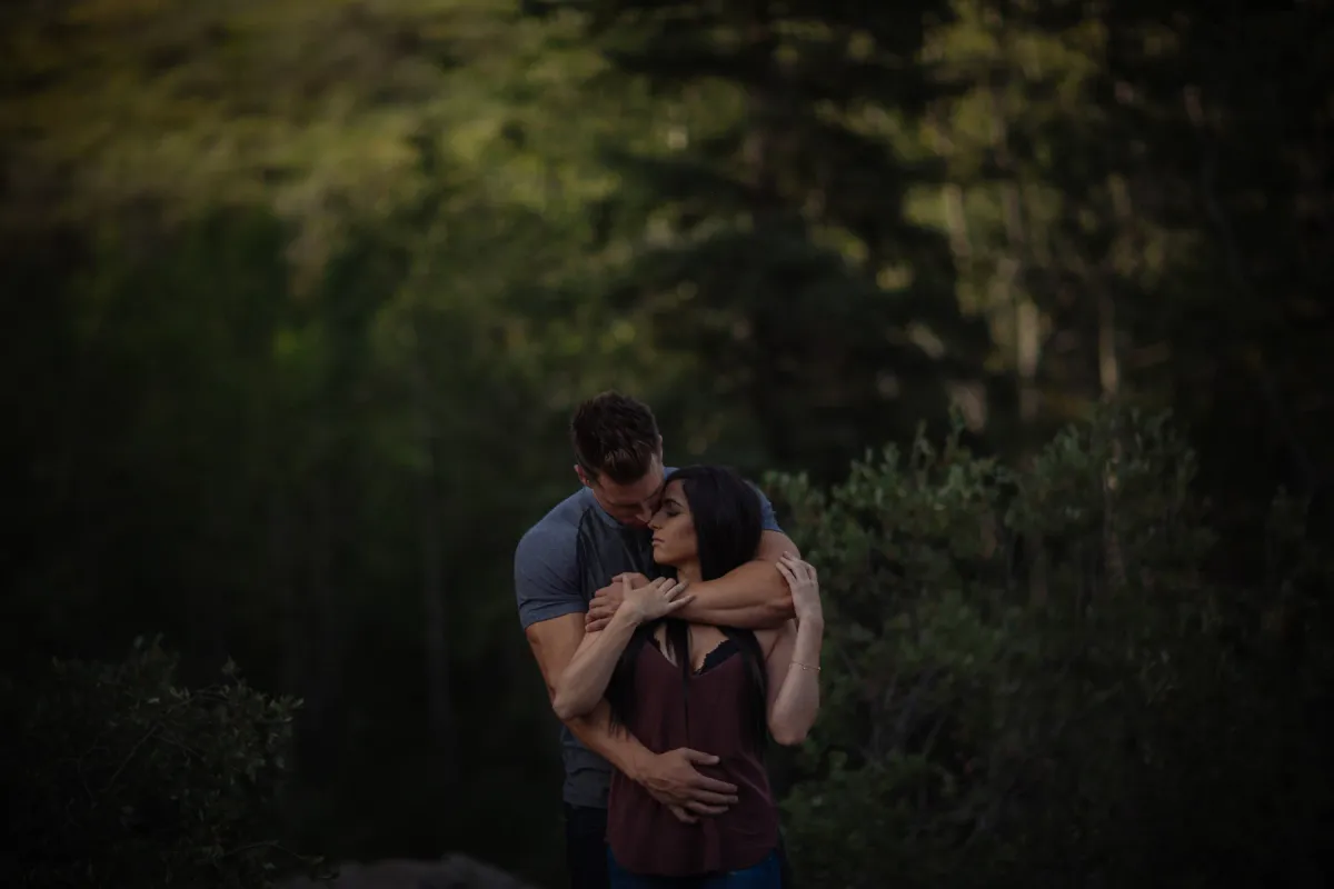 Couple sitting close together in the woods during an engagement session