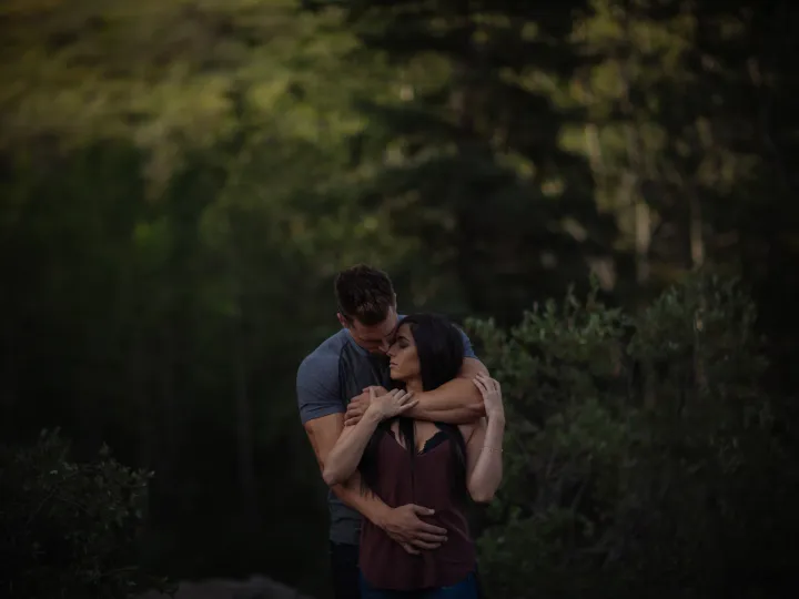 Couple sitting close together in the woods during an engagement session