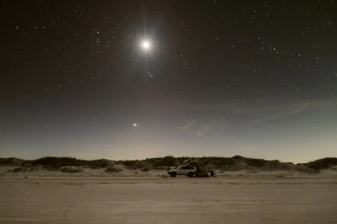 Small moon above a dark sandy landscape at night