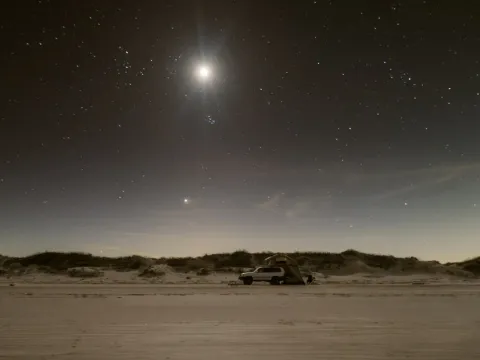 Small moon above a dark sandy landscape at night