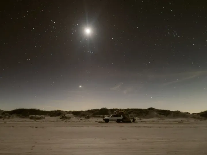 Small moon above a dark sandy landscape at night