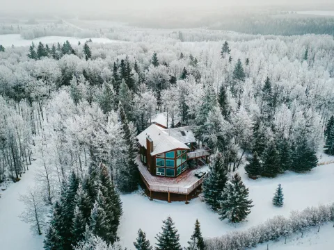 Aerial winter view of a small cabin surrounded by snow-covered evergreens