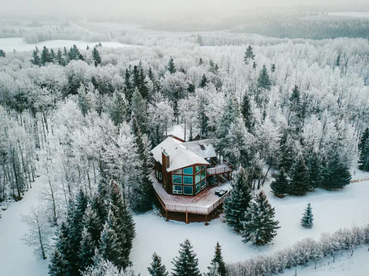 Aerial winter view of a small cabin surrounded by snow-covered evergreens