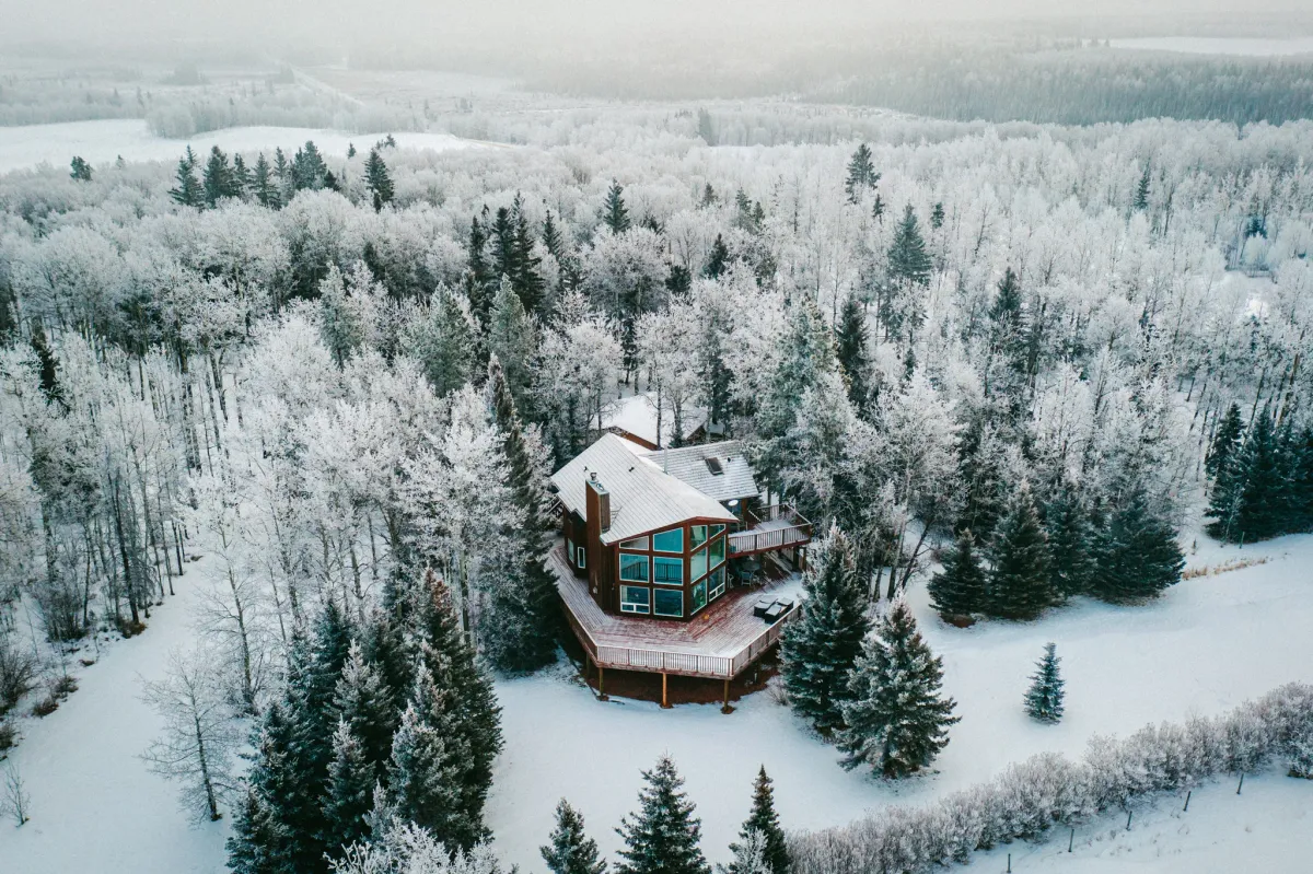 Aerial winter view of a small cabin surrounded by snow-covered evergreens