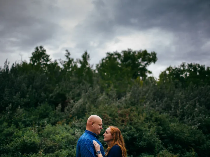 Couple standing together below storm clouds and forest trees