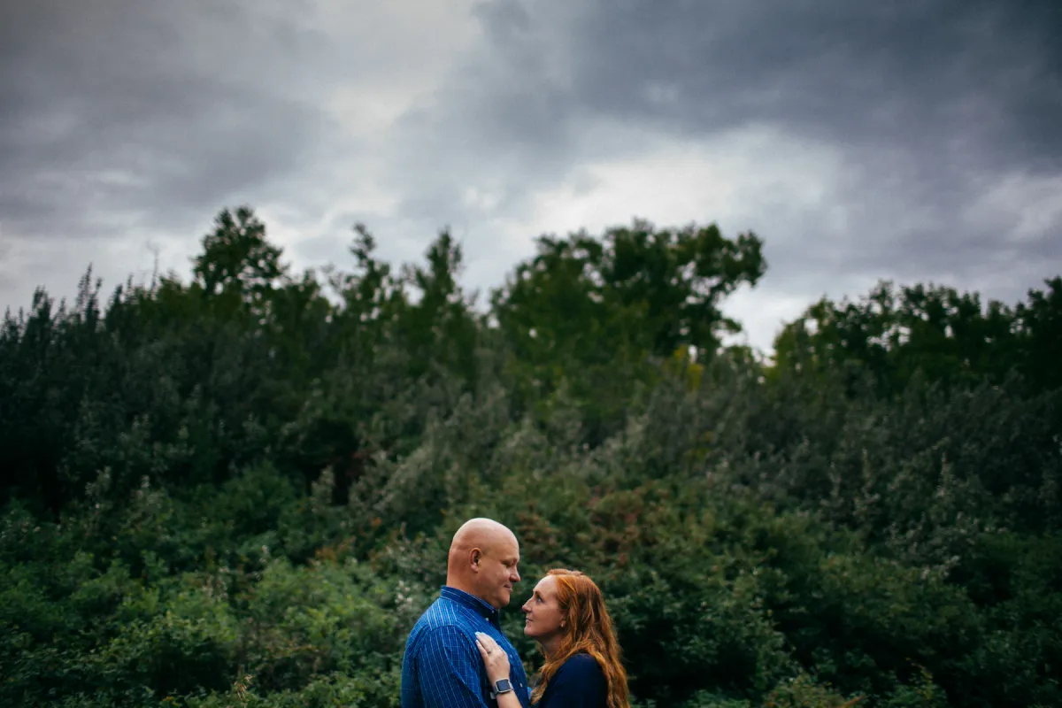 Couple standing together below storm clouds and forest trees