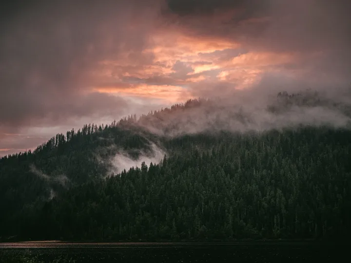 Pink storm clouds breaking over dark forested hills at sunset