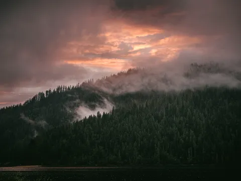 Pink storm clouds breaking over dark forested hills at sunset