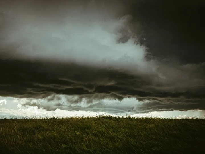 Dark storm cloud moving over a green prairie field