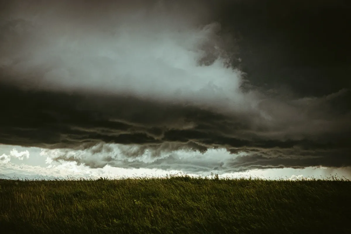 Dark storm cloud moving over a green prairie field