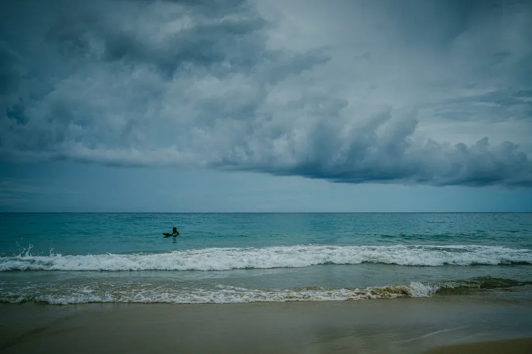 Surfer in dark ocean water beneath a storm cloud