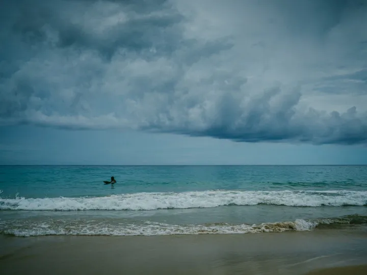 Surfer in dark ocean water beneath a storm cloud