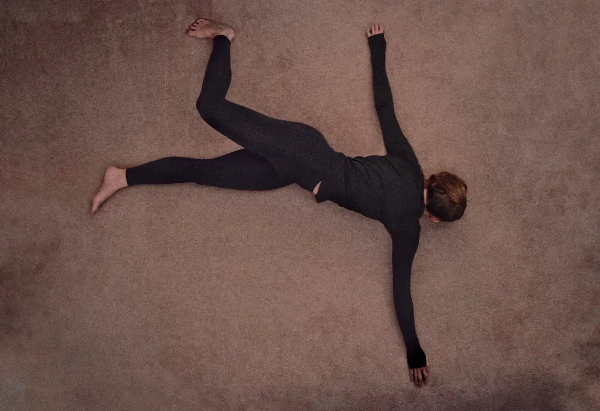 Dancer lying on a muted floor with arms and legs extended in an expressive pose