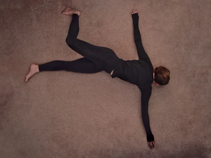 Dancer lying on a muted floor with arms and legs extended in an expressive pose