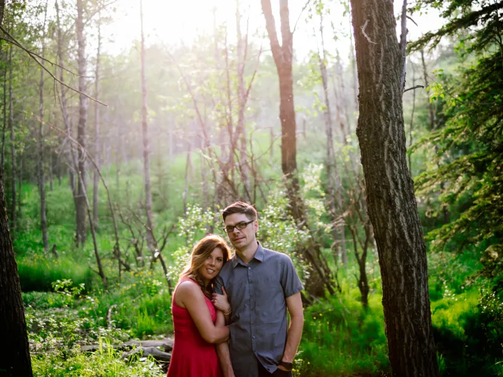 Couple smiling together in sunlit pine trees during an engagement session
